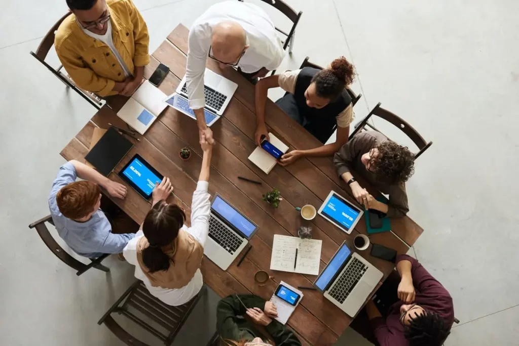 Gemeinsame Projektbesprechung bei Sofinity in Landsberg am Lech – Team aus vier Frauen und vier Männern mit symbolischem Handschlag am Konferenztisch